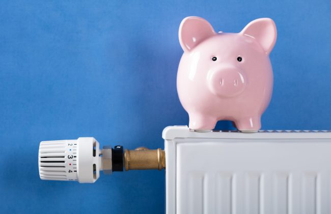 Close-up,Of,Piggy,Bank,On,Heating,Radiator,Against,Blue,Background